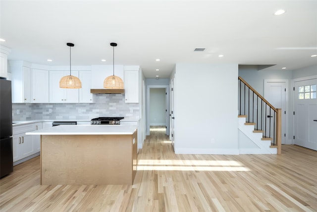 kitchen featuring tasteful backsplash, freestanding refrigerator, light wood-style floors, light countertops, and white cabinetry