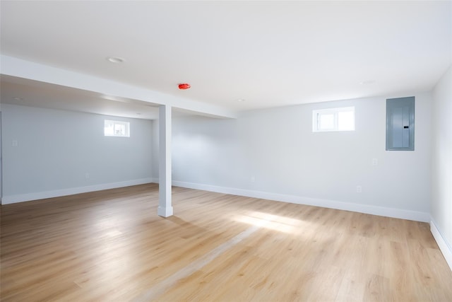 below grade area with electric panel, light wood-style floors, a healthy amount of sunlight, and baseboards