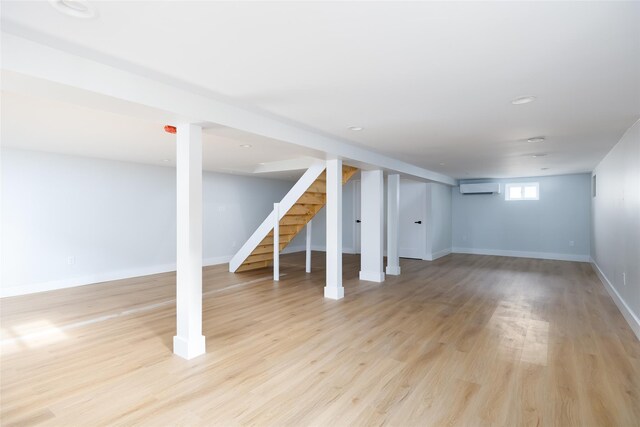 below grade area featuring stairs, baseboards, a wall mounted AC, and light wood-style floors
