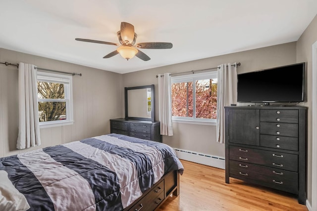bedroom featuring a ceiling fan, light wood-style floors, multiple windows, and a baseboard radiator