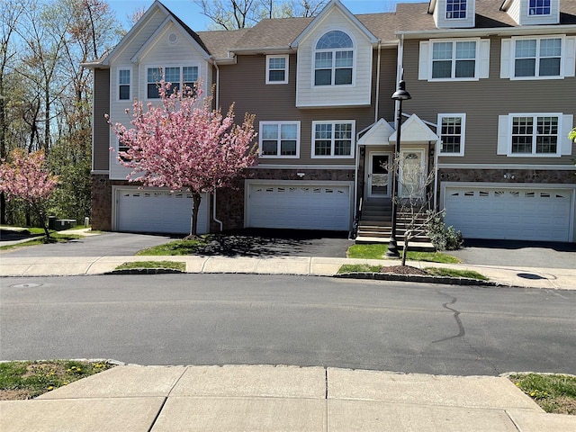 townhome / multi-family property with driveway, stone siding, and a garage