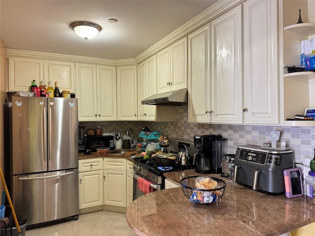 kitchen featuring a sink, under cabinet range hood, decorative backsplash, dark stone countertops, and appliances with stainless steel finishes