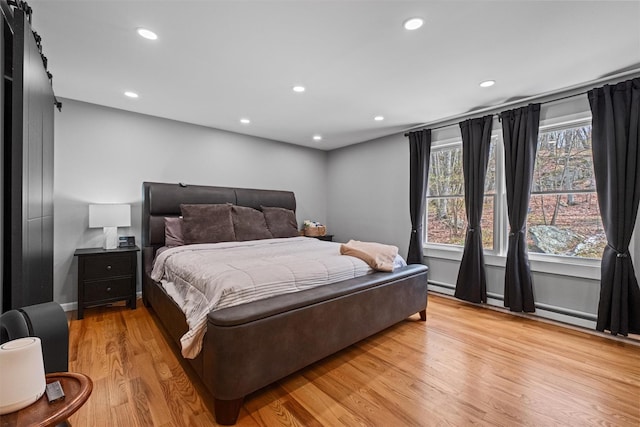 bedroom featuring baseboard heating, recessed lighting, a barn door, and light wood-style flooring