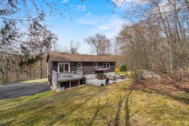 back of property with a patio, a wooden deck, a lawn, and roof with shingles