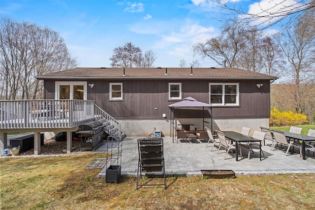 back of house featuring a patio, a wooden deck, a shingled roof, and a lawn