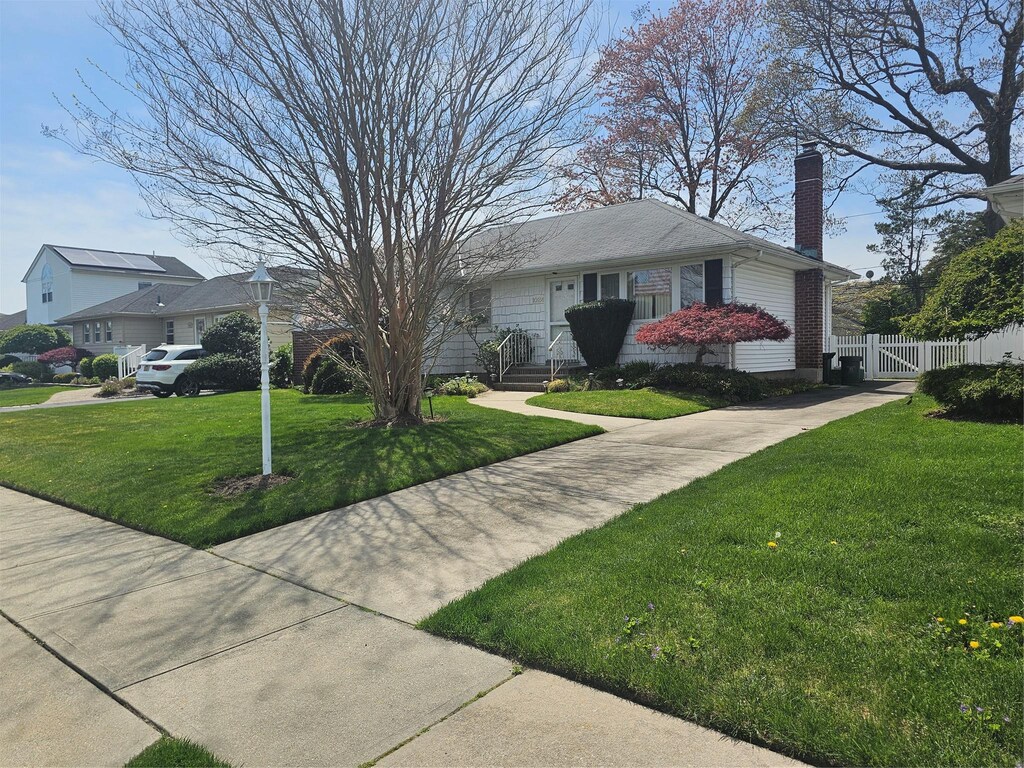 view of front facade featuring a chimney, fence, and a front lawn