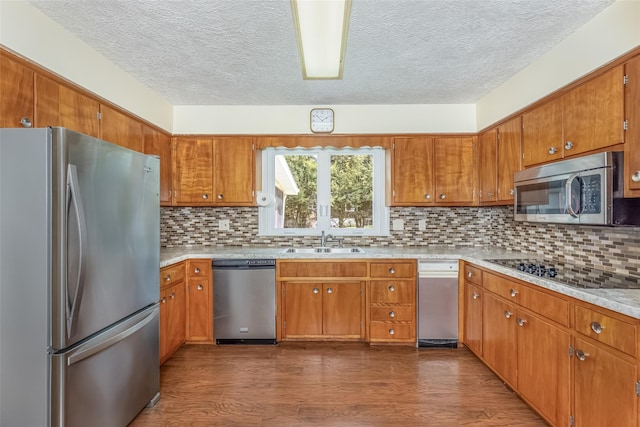 kitchen with appliances with stainless steel finishes, a sink, light countertops, a textured ceiling, and brown cabinetry
