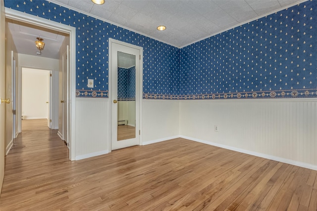 unfurnished room with attic access, crown molding, wood finished floors, a wainscoted wall, and wallpapered walls