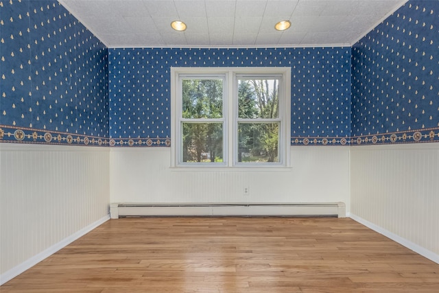 additional living space featuring wallpapered walls, a baseboard heating unit, wood finished floors, and a wainscoted wall