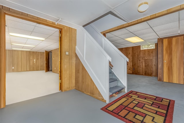 basement featuring stairs, wood walls, and a drop ceiling