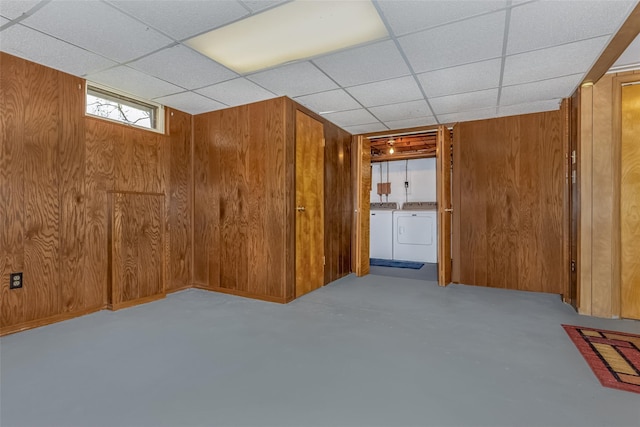 basement featuring separate washer and dryer, wood walls, and a drop ceiling