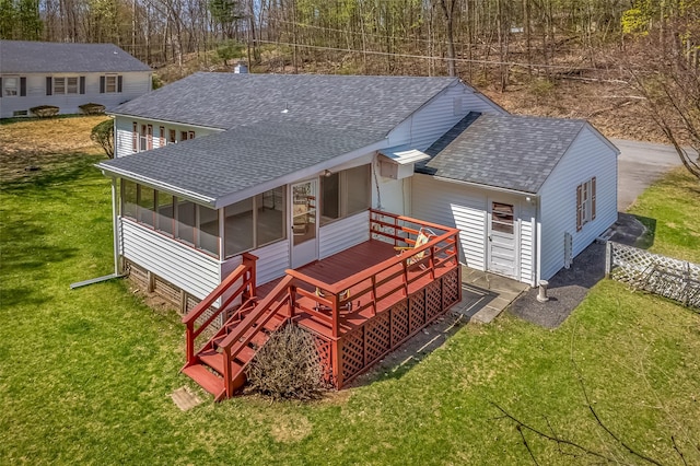 back of house featuring a yard, a sunroom, roof with shingles, and a deck