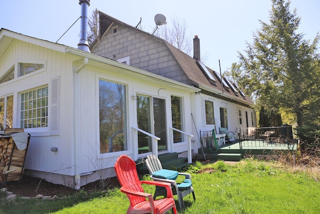 rear view of property with a chimney, a deck, a shingled roof, and a lawn
