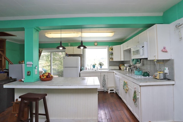 kitchen featuring white cabinetry, a kitchen bar, ornamental molding, and white appliances