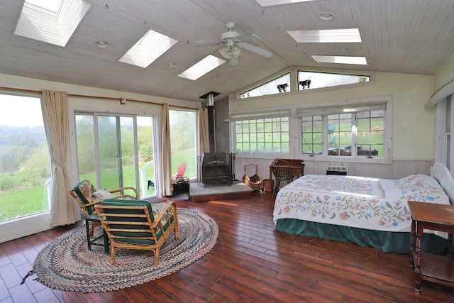 bedroom featuring wainscoting, wooden walls, a wood stove, hardwood / wood-style floors, and vaulted ceiling with skylight