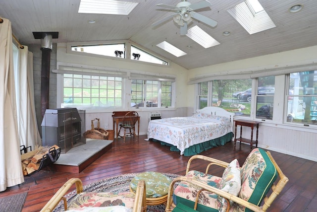 bedroom with a wood stove, wood-type flooring, a skylight, and high vaulted ceiling