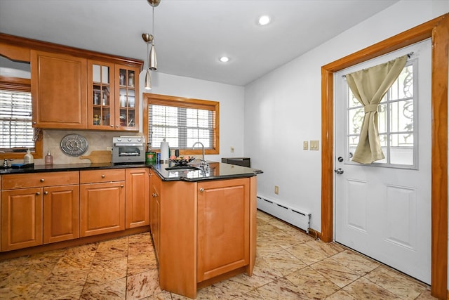 kitchen with glass insert cabinets, a baseboard heating unit, a sink, pendant lighting, and a peninsula
