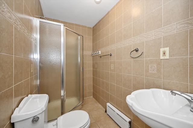 bathroom with a sink, a stall shower, baseboard heating, toilet, and tile walls