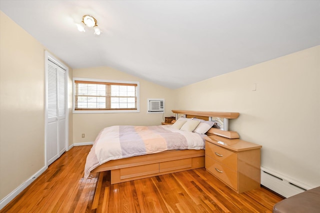 bedroom with a baseboard heating unit, a closet, light wood-type flooring, vaulted ceiling, and a wall mounted air conditioner
