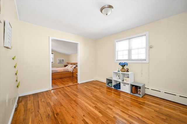 unfurnished room with baseboard heating, wood finished floors, and baseboards