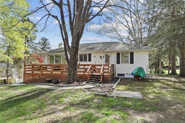rear view of house with a chimney, a deck, and a lawn