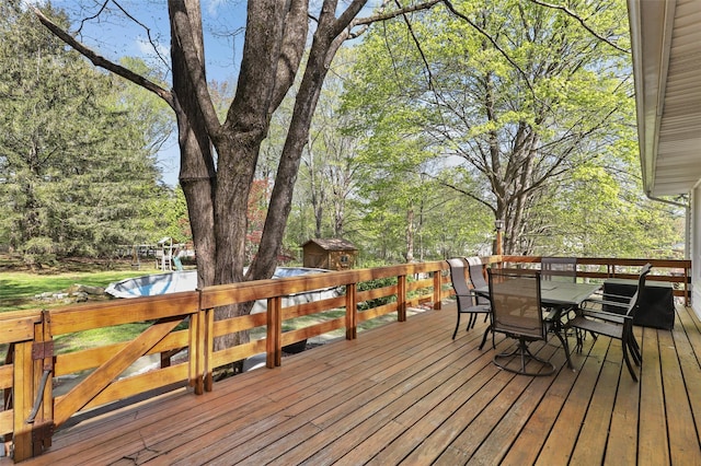 wooden terrace with an outdoor structure, outdoor dining space, and a storage unit