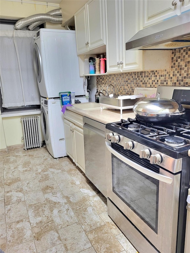 kitchen featuring stainless steel appliances, under cabinet range hood, stacked washer and clothes dryer, tasteful backsplash, and radiator heating unit