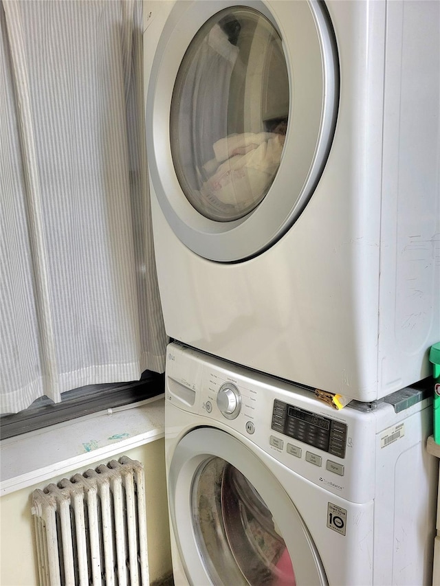 laundry area with stacked washer and dryer, radiator heating unit, and laundry area