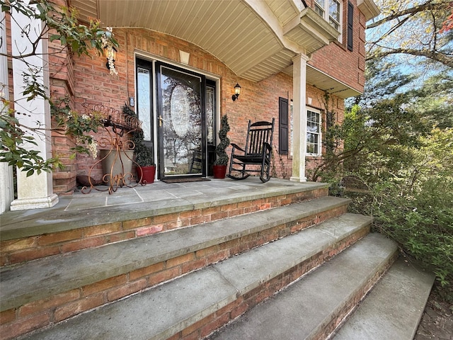doorway to property featuring a porch and brick siding