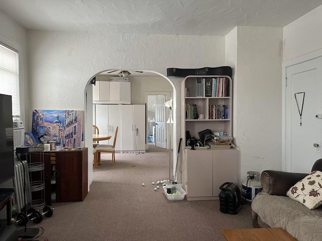 living room featuring arched walkways, carpet flooring, ceiling fan, and a textured wall