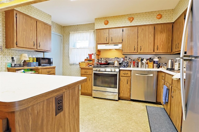 kitchen with light floors, wallpapered walls, under cabinet range hood, appliances with stainless steel finishes, and light countertops