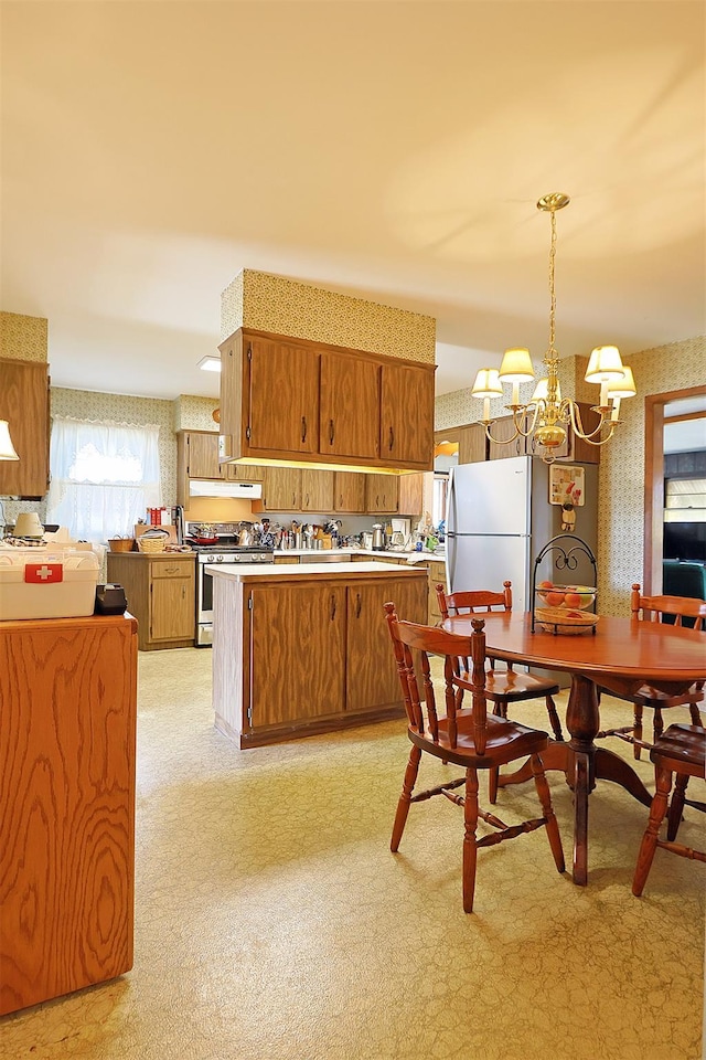 kitchen featuring brown cabinets, wallpapered walls, stainless steel gas range oven, and freestanding refrigerator