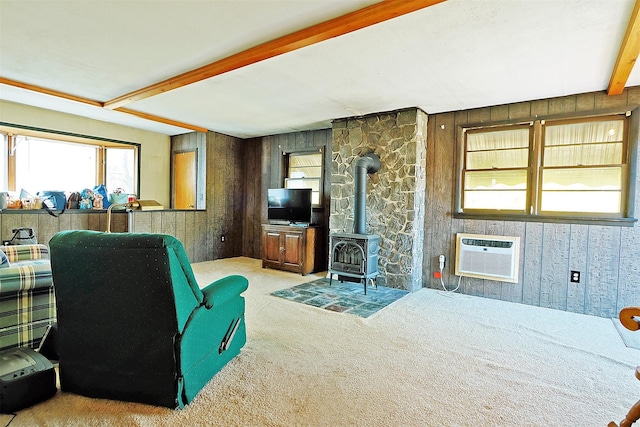 carpeted living area featuring wooden walls, a wood stove, a wall mounted AC, and beam ceiling