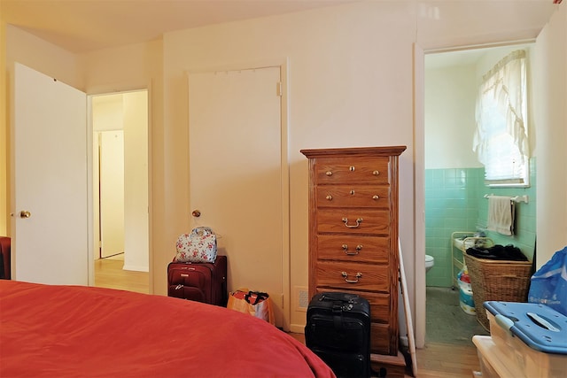 bedroom with connected bathroom, tile walls, and wood finished floors