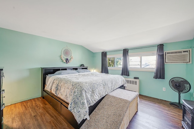 bedroom featuring an AC wall unit, radiator heating unit, vaulted ceiling, and wood finished floors