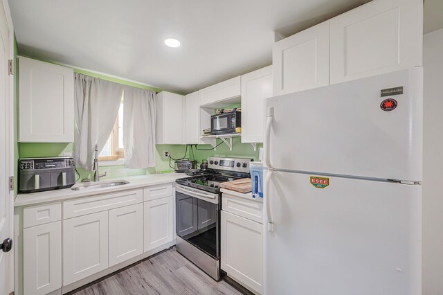 kitchen with stainless steel electric range oven, freestanding refrigerator, a sink, white cabinetry, and black microwave