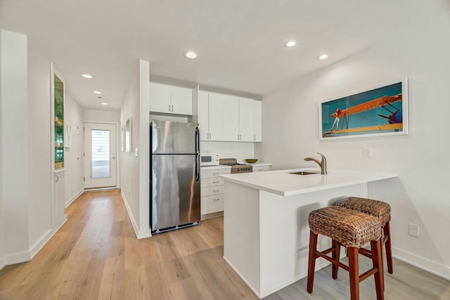 kitchen with freestanding refrigerator, light wood-style floors, a breakfast bar area, and white microwave