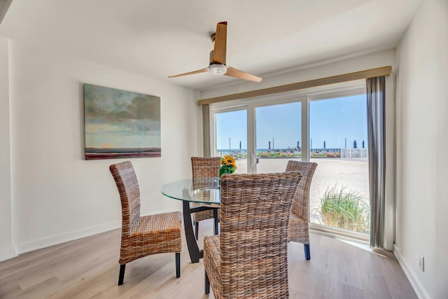 dining area with baseboards, light wood-style flooring, ceiling fan, and a water view