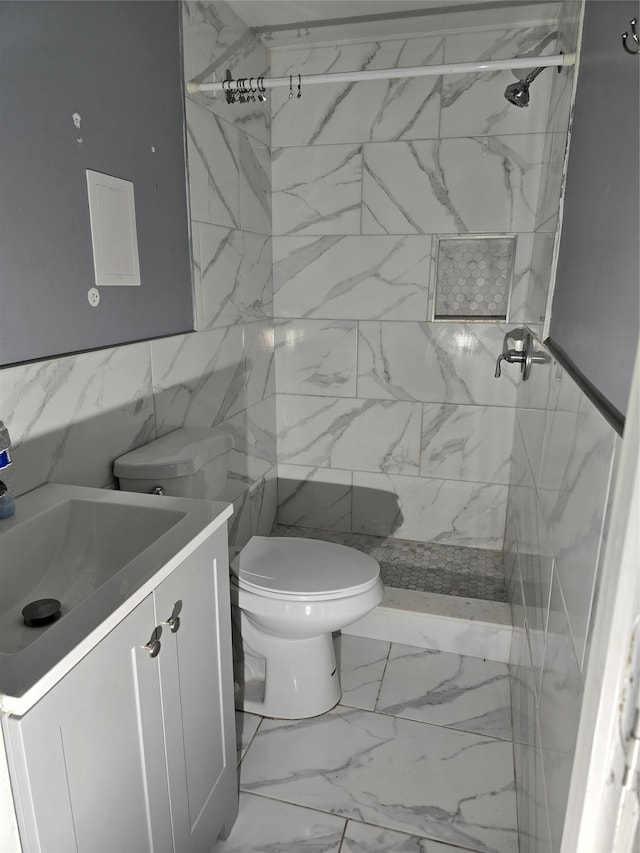 full bathroom featuring toilet, marble finish floor, tiled shower, and vanity