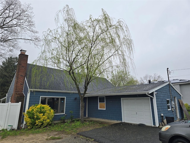 single story home featuring aphalt driveway, a chimney, a shingled roof, an attached garage, and fence