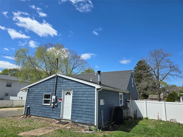 back of house with fence, heating fuel, and roof with shingles