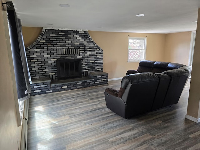 living room with a brick fireplace, baseboards, and wood finished floors