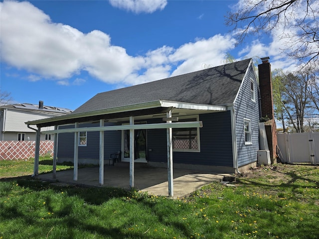 back of property with fence, roof with shingles, a chimney, a patio area, and a lawn
