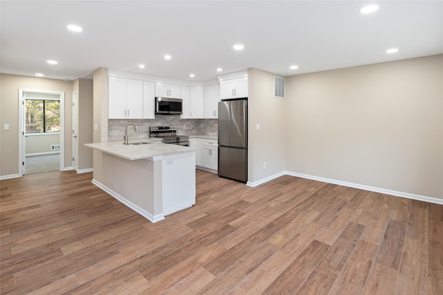 kitchen featuring a peninsula, baseboards, a sink, appliances with stainless steel finishes, and backsplash