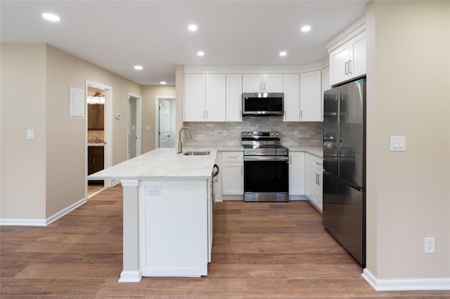 kitchen with a peninsula, white cabinetry, a sink, appliances with stainless steel finishes, and backsplash