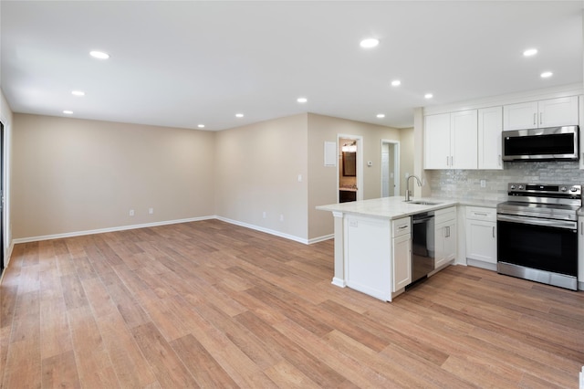 kitchen featuring white cabinets, a sink, stainless steel appliances, a peninsula, and light wood-type flooring
