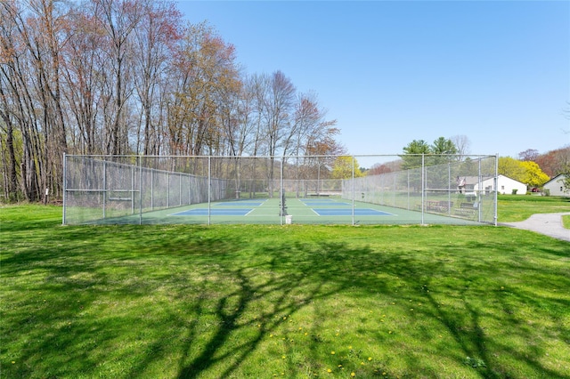 view of tennis court featuring fence and a yard