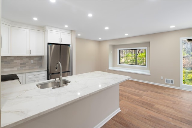kitchen with decorative backsplash, visible vents, light stone countertops, a sink, and freestanding refrigerator