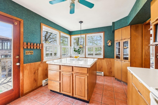 kitchen with wainscoting, a ceiling fan, a baseboard heating unit, and tile countertops