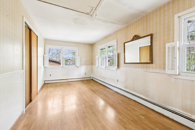 unfurnished bedroom featuring a baseboard heating unit, multiple windows, and wood finished floors